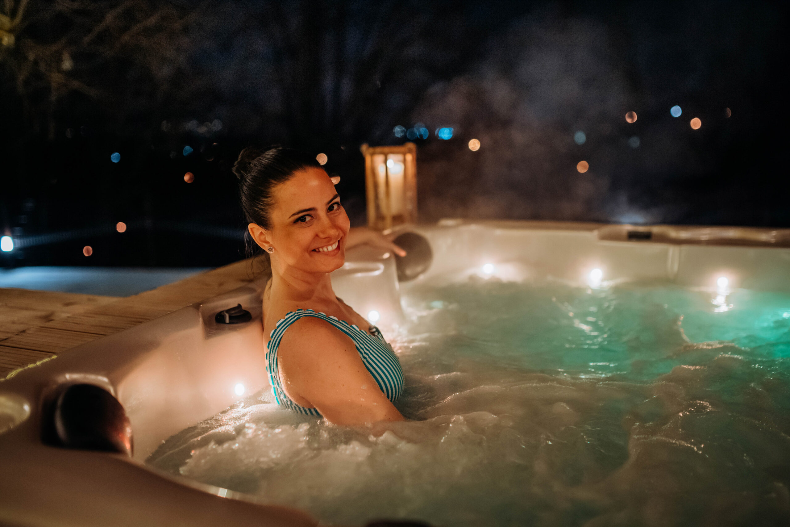 Young woman enjoying outdoor bathtub in her terrace during cold winter evening.